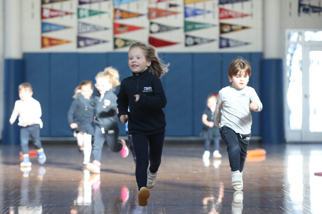 Pre-K running in gym with college flags in background